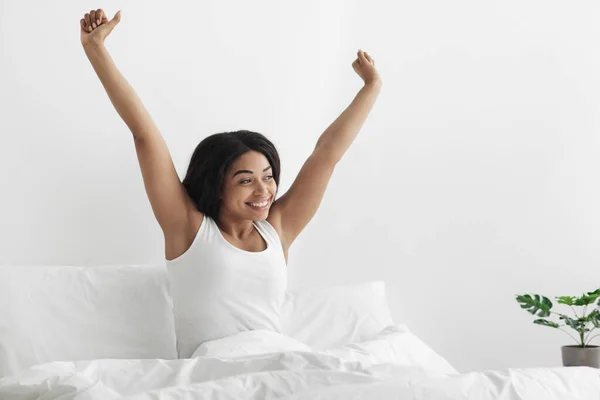 Nový den a skvělá nálada. Mladá dobře spící Afroameričanka sedí na posteli a protahuje se, volný prostor — Stock fotografie