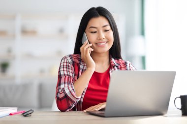 Telekomünikasyon konsepti. Genç Koreli Kadın Cep Telefonu Konuşuyor ve Dizüstü bilgisayar kullanıyor