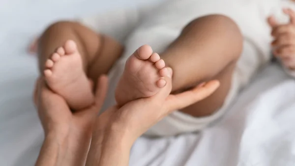 Afrika kökenli küçük sevimli bir Amerikalı bebeğin ayaklarını tutan kadının yakın çekimi. — Stok fotoğraf