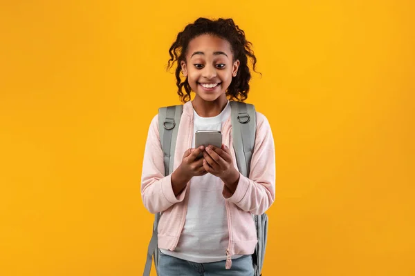 Захоплена чорна дівчина використовує мобільний телефон в жовтій студії — стокове фото