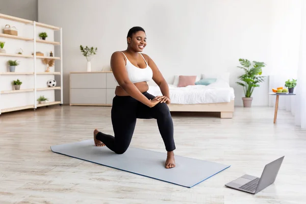 Longitud completa de la mujer negra con sobrepeso haciendo ejercicio de vídeo deportivo en línea en el ordenador portátil en casa —  Fotos de Stock