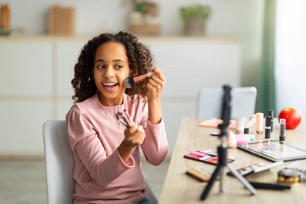 Beleza blogging. Alegre Africano americano adolescente gravação cosméticos produto revisão, usando telefone no tripé — Fotografia de Stock