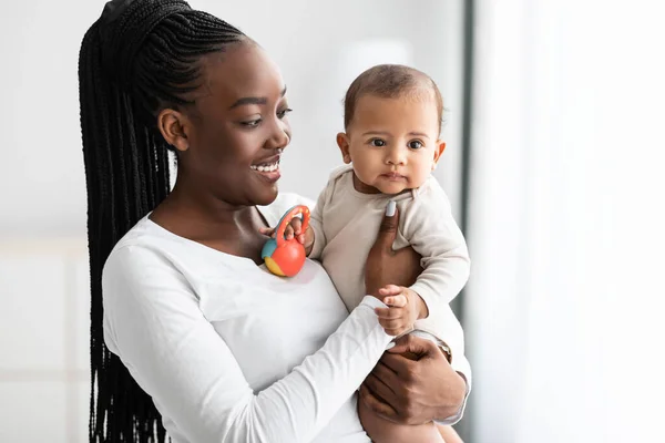 Afrika kökenli Amerikalı anne oyuncağıyla oynayan tatlı bebeğine sarılıyor. — Stok fotoğraf