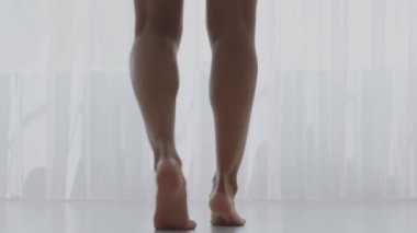 Sağlıklı bir yaşam tarzı ve harika bir sabah havası. Genç, tanınmayan, sağlıklı bacakları olan, evde dans eden siyah bir kadın.