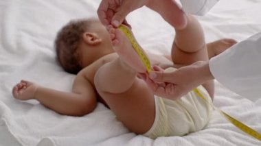 Aylık tıbbi muayene. Bebek ayağını mezurayla ölçen bir pediyatrist. Yatakta yatan tatlı siyah bir bebek.