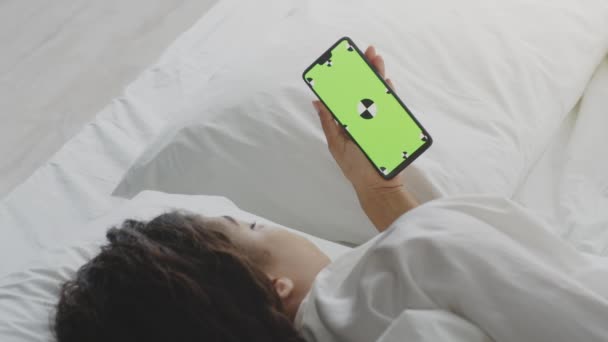 Mujer afroamericana joven viendo televisión digital en el teléfono inteligente, acostado en la cama, teléfono con pantalla clave de croma verde — Vídeos de Stock