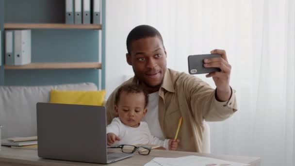 Glückliche Elternschaft. Junger stolzer afrikanisch-amerikanischer Vater macht Selfie mit entzückendem lockigem Baby-Sohn, der aus der Ferne arbeitet — Stockvideo