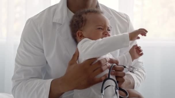 Stressvolle medische afspraak. Llittle afrikaanse amerikaanse baby jongen huilen op artsen handen, het gevoel ongemakkelijk — Stockvideo