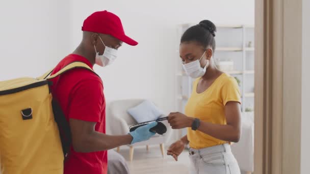 Jeune femme afro-américaine isolée dans un masque médical protecteur payant par carte de crédit pour la livraison d'épicerie — Video