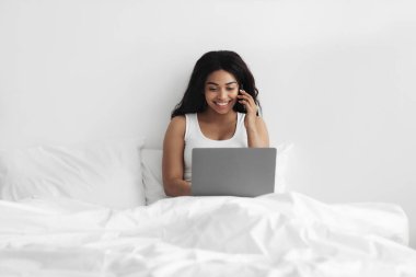 Her zaman görüşüyoruz. Genç Afrikalı Amerikalı kadın yatakta oturuyor, dizüstü bilgisayarla çalışıyor ve cep telefonuyla konuşuyor.