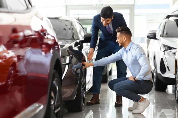 Hombre árabe joven eligiendo coche deportivo en sala de exposición —  Fotos de Stock