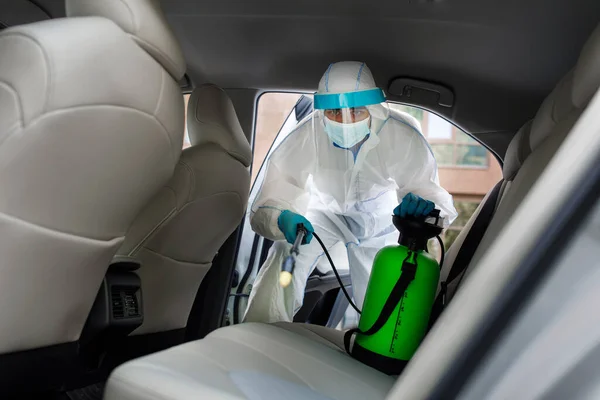 Employer in protective suit with mask disinfecting inside car — Stock Photo, Image