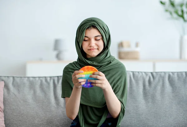 可爱的印度少女穿着头巾，玩着明亮的POP IT玩具，在家里玩着有趣的减压游戏的肖像 — 图库照片