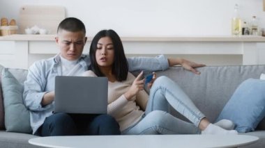 Memnuniyetsiz Asyalı çift evde dizüstü bilgisayar ve kredi kartı kullanıyor.