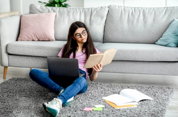 Indiano teen girl lettura del libro di testo, seduto sul pavimento con computer portatile e materiali di studio, imparare a distanza da casa — Foto Stock