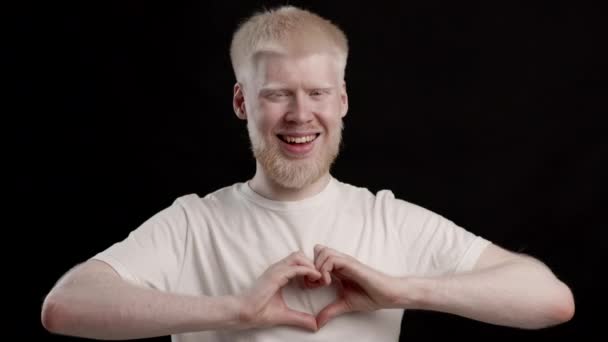 Albino Guy gesticolando forma di cuore con le dita, sfondo nero — Video Stock