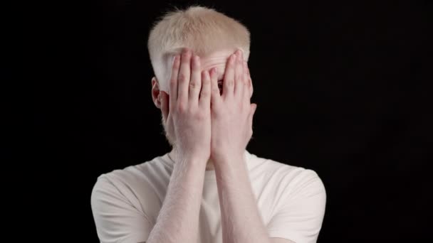 Albino uomo che copre il viso sbirciando attraverso le dita su sfondo nero — Video Stock