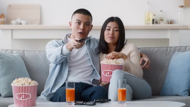 Японская пара смотрит телевизор, сидя на диване дома — стоковое видео