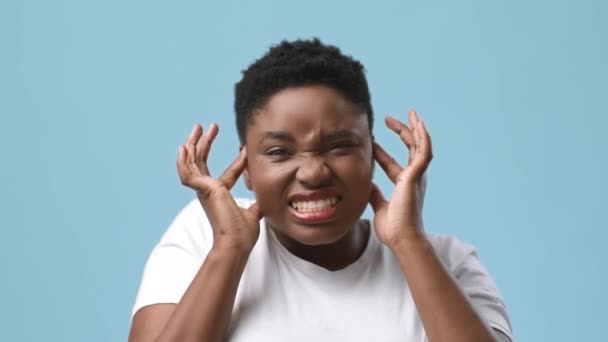 Mujer africana teniendo dolor de cabeza, masaje templos cubriendo oídos, fondo azul — Vídeos de Stock