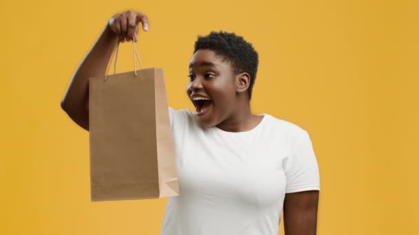 Emotionele Afro-Amerikaanse vrouw met papieren shopper tas, gele achtergrond — Stockvideo