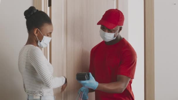 Delivery and protection. Black woman in disposable mask using smartwatch for contactless payment for grocery order — Video