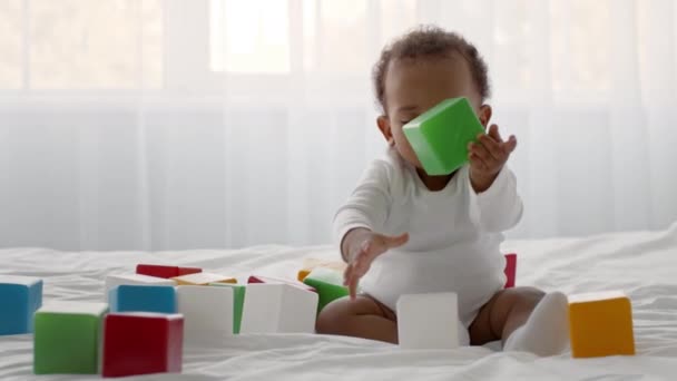 Cute little curly african american baby boy playing with colorful blocks, sitting on bed, tracking shot, slow motion — Stock Video