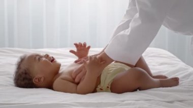 Bebek gelişimi. Yeni doğmuş Afro-Amerikan bebeğine masaj yapan masör. Yatakta yatan ve prosedürlerin tadını çıkaran çocuk.