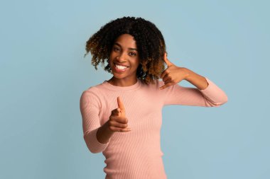 Ara beni. Siyah kadın, kulak dibinde elini tutuyor ve kamerayı işaret ediyor.