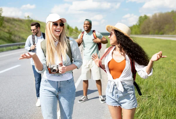 Gruppo di amici multinazionali millenari che camminano lungo l'autostrada, chattano, ridono, si divertono — Foto Stock