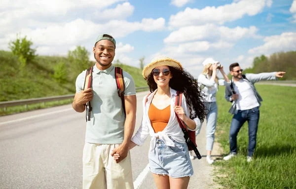 Svart kille och hans flickvän reser tillsammans med olika vänner, promenader längs asfalterad väg, liftar på sommaren — Stockfoto