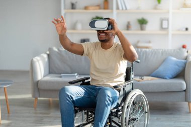 Tekerlekli sandalyedeki engelli genç adam evde VR gözlükleriyle artırılmış gerçekliği keşfediyor.