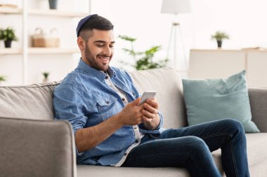 Rahat koltukta oturan gülümseyen Yahudi adam cep telefonu kullanıyor.