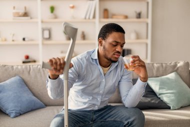Depresyon, kriz konsepti. Koltukta oturan mutsuz siyah adam, evde alkol içiyor.