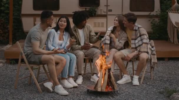 Grupo de amigos multiculturales sentados alrededor de la hoguera en el camping y el chat — Vídeos de Stock