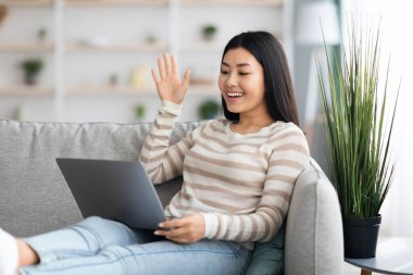 Neşeli genç Asyalı kadın laptopla evde video görüşmesi yapıyor.