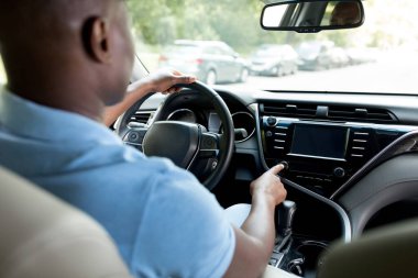 Siyah adam test sürüşü yapıyor, müziği açıyor, arka planda