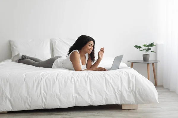 Mujer joven negro que tiene videollamada en el ordenador portátil mientras está acostado en la cama en casa el fin de semana por la mañana, espacio para copiar —  Fotos de Stock