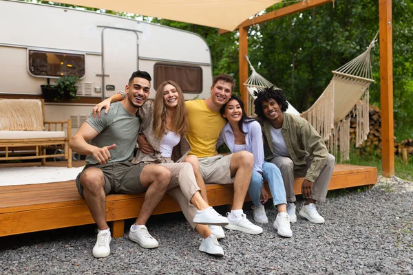Portrait complet de jeunes amis multiraciaux assis près du camping-car, souriant à la caméra à l'extérieur — Photo