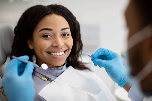 Retrato de una paciente negra sonriente que recibe tratamiento dental con estomatólogo — Foto de Stock