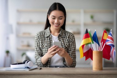 Neşeli Asyalı genç bayan cep telefonu kullanıyor, İngilizce dersi alıyor.