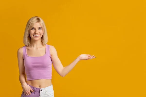 Anuncio de productos de belleza. Feliz dama sosteniendo producto de cuidado de la piel invisible en su mano, posando sobre fondo amarillo —  Fotos de Stock