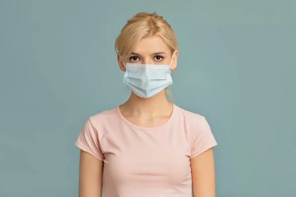 Gezondheidszorgconcept. Portret van jonge vrouw met chirurgisch masker geïsoleerd op grijze studio muur achtergrond — Stockfoto
