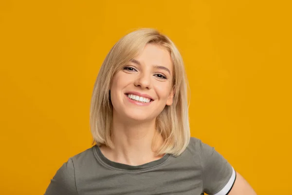 Γυναικείο πορτρέτο. Ευτυχισμένη νεαρή γυναίκα με ξανθά μαλλιά κοιτάζοντας την κάμερα και χαμογελώντας, ποζάροντας στο στούντιο, κίτρινο φόντο — Φωτογραφία Αρχείου