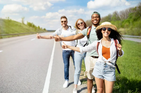 Jovens amigos multirraciais em pé na estrada, mostrando carona gesto, parar de carro, indo em viagem juntos — Fotografia de Stock