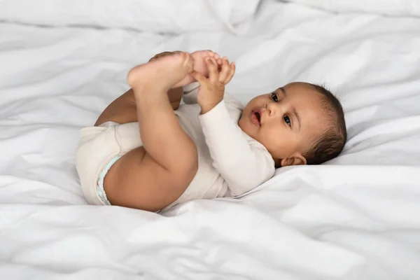 Bebê afro-americano bonito deitado na cama e brincando — Fotografia de Stock