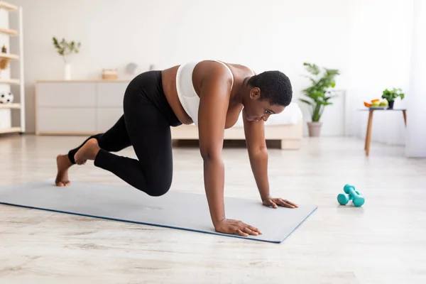 Ejercicios efectivos de peso corporal. Mujer negra curvilínea haciendo ejercicio de fuerza, corriendo con las manos en el suelo en casa —  Fotos de Stock