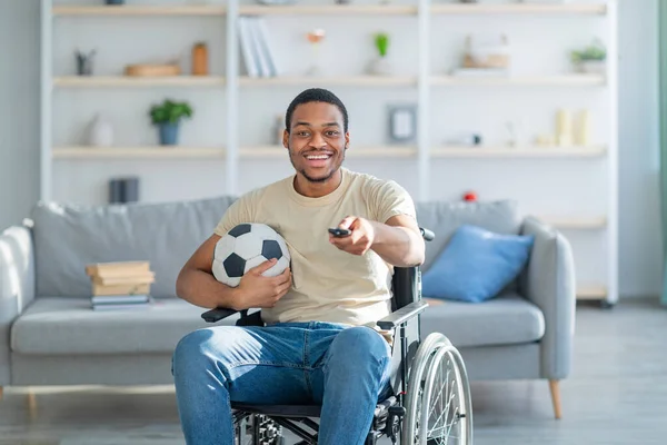 坐在轮椅上的快乐的受损黑人在家里看电视足球赛 — 图库照片