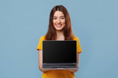 Güzel genç bayan boş ekranlı dizüstü bilgisayar gösteriyor.