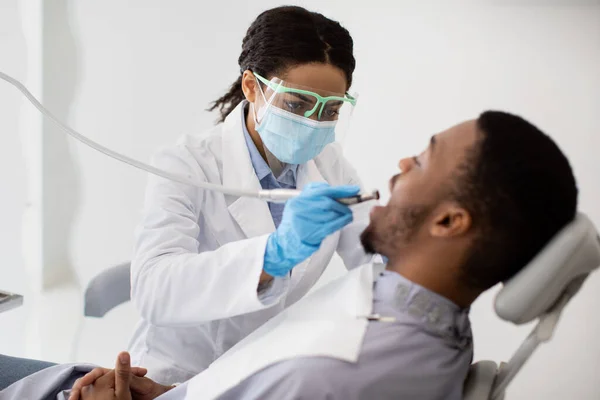 Dentista Senhora na máscara médica que trata os pacientes do sexo masculino dentes com broca dentária — Fotografia de Stock