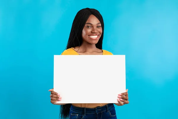 Mulher negra alegre mostrando texto de publicidade de pôster vazio, fundo azul — Fotografia de Stock